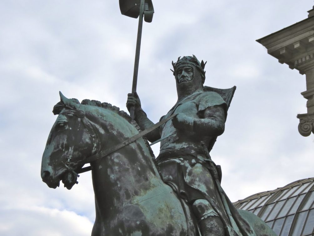 Green copper statue of knight on a horse with a lance