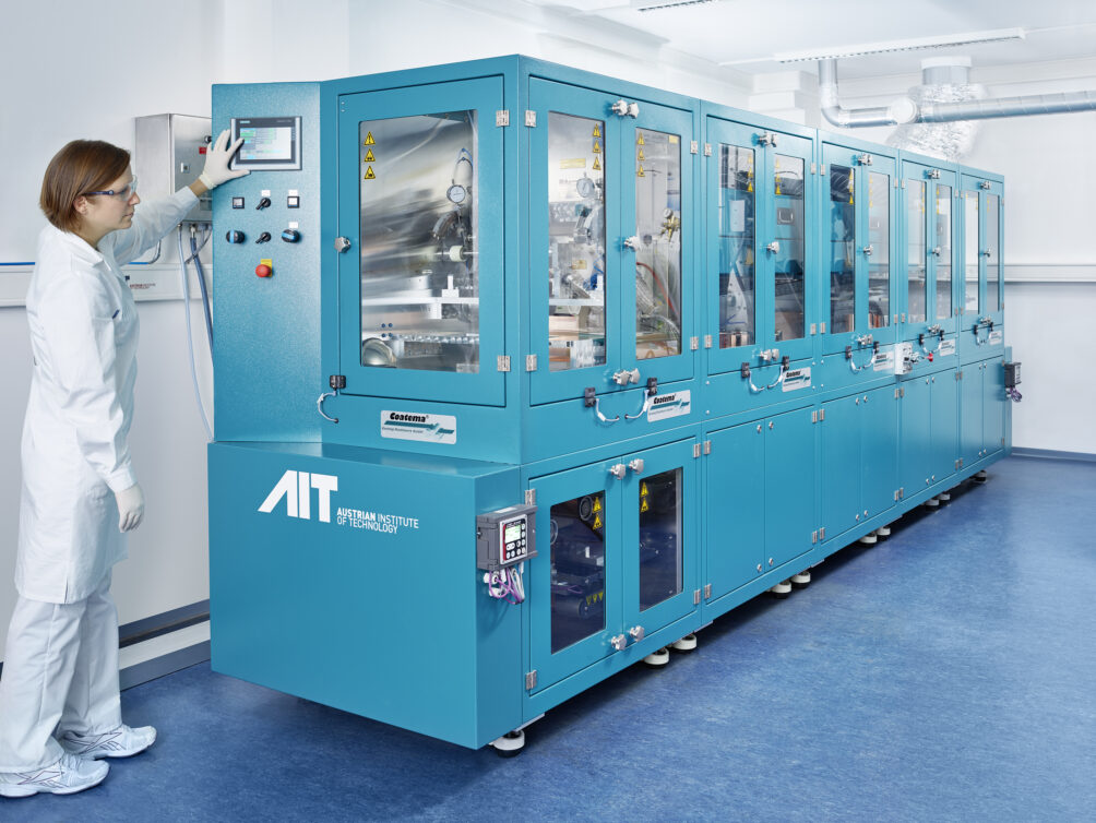 Woman in white lab gear pushing a button on large piece of blue lab equipment